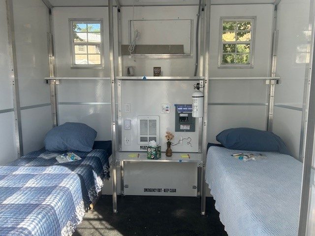 Inside a tiny shelter: two made beds under a window